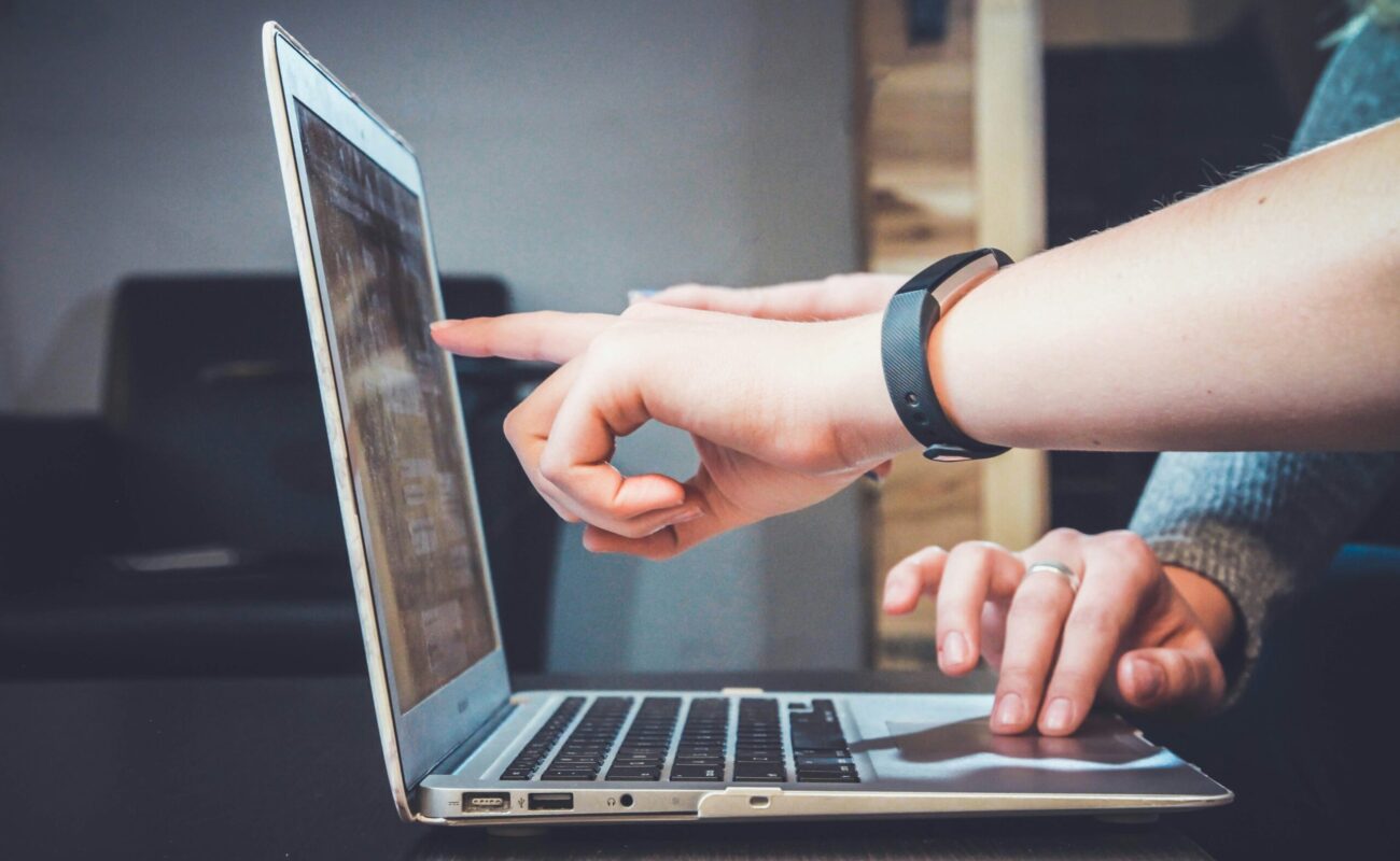 Zwei hände zeigen auf einen Laptop Bildschirm während eine Andere Hand das Trackpad bedient