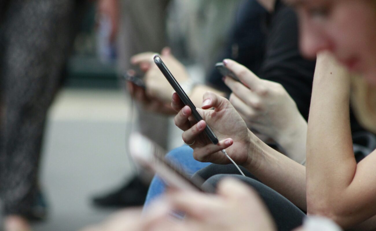 Hände von Jugendlichen, die nebeneinander sitzen und alle am Handy sind