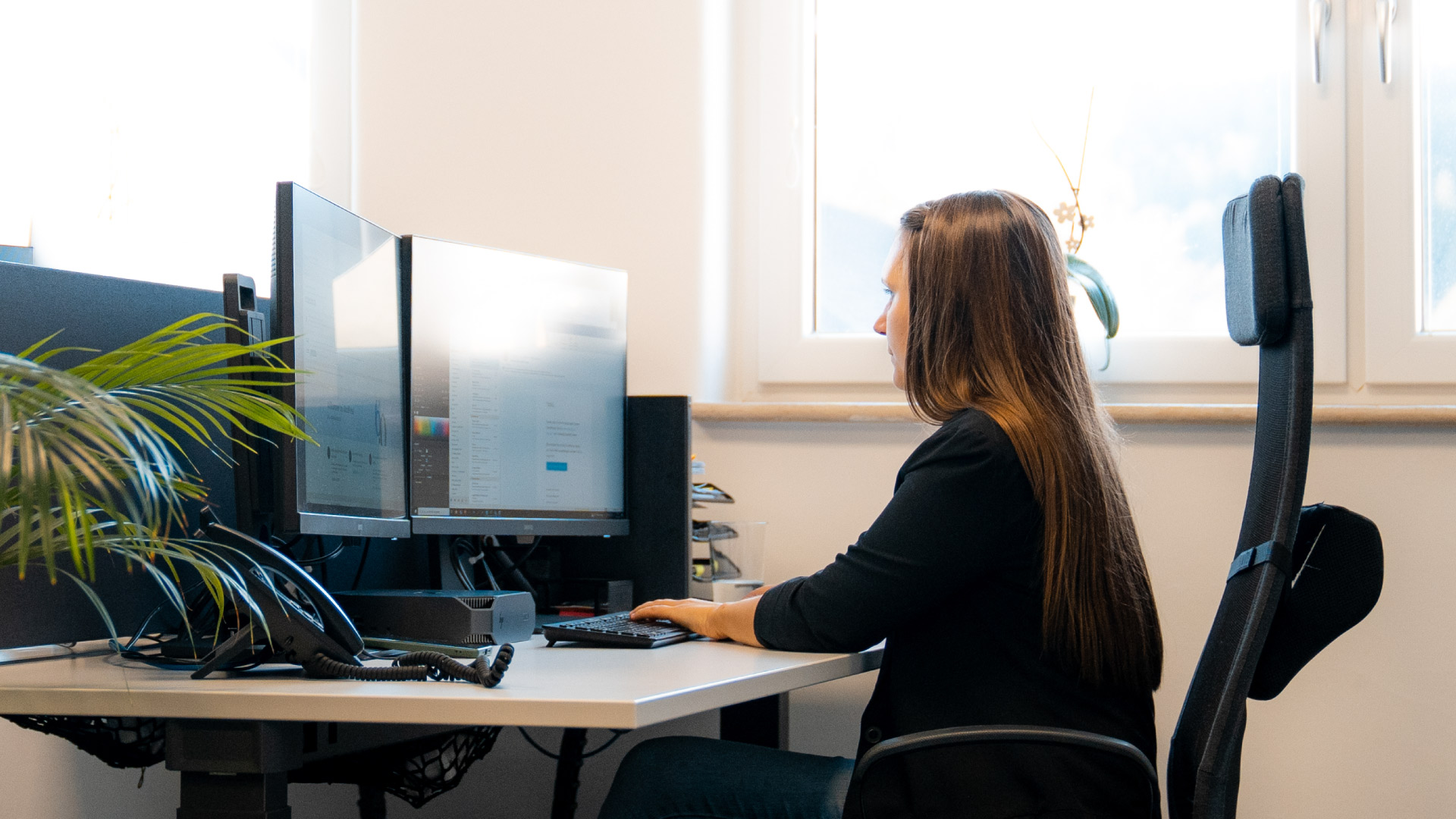 Mitarbeiterin arbeitet am Schreibtisch mit zwei Monitoren im hellen Büro
