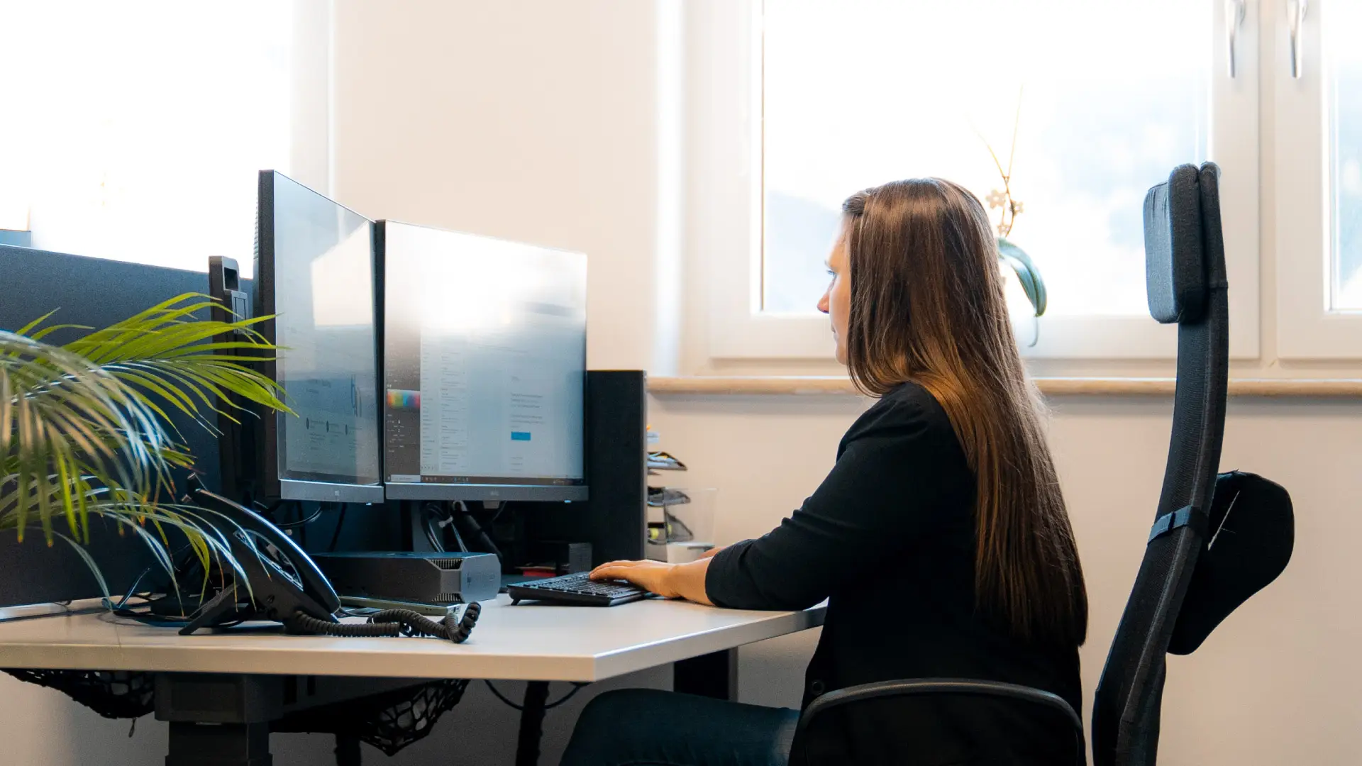 Mitarbeiterin arbeitet am Schreibtisch mit zwei Monitoren im hellen Büro