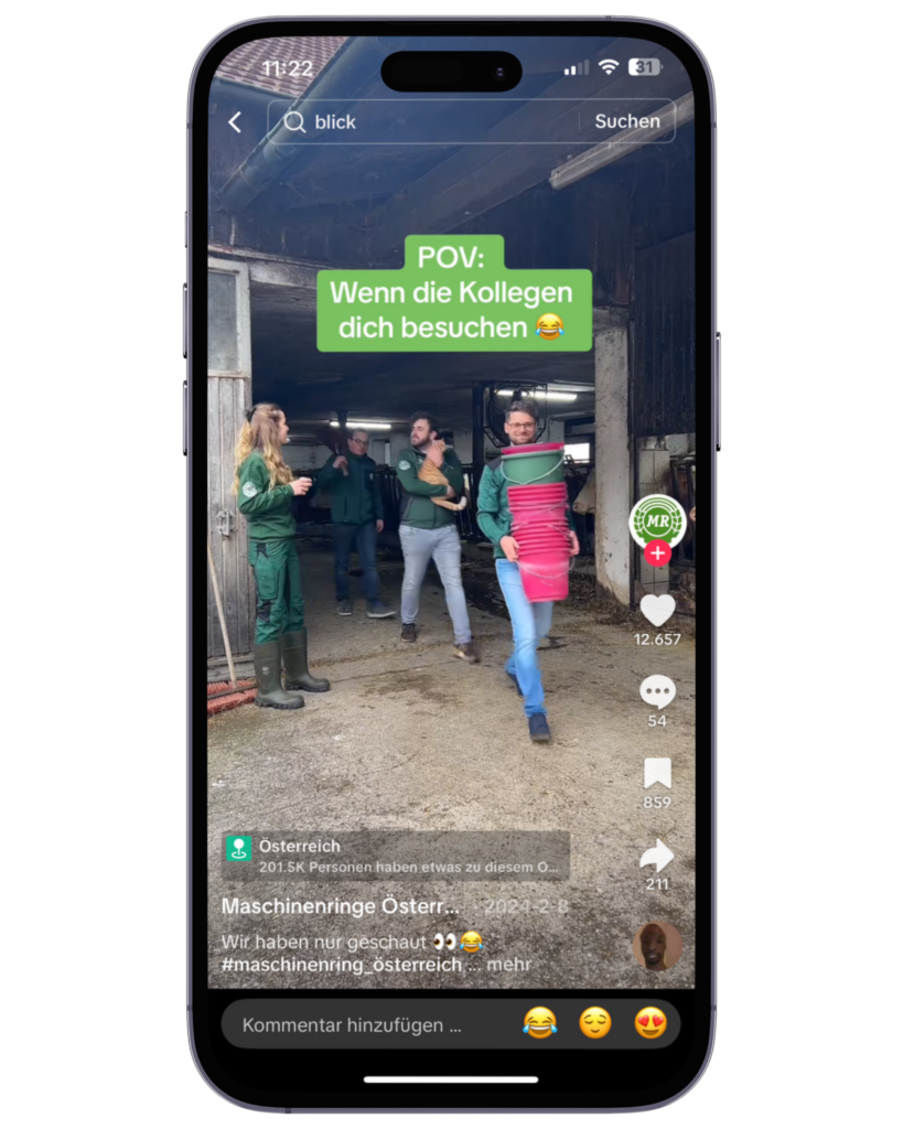 Ein TikTok-Video wird auf einem Smartphone gezeigt. Darin sind mehrere Personen in Arbeitskleidung vor einem Stall zu sehen, eine Person trägt eine Schürze.
