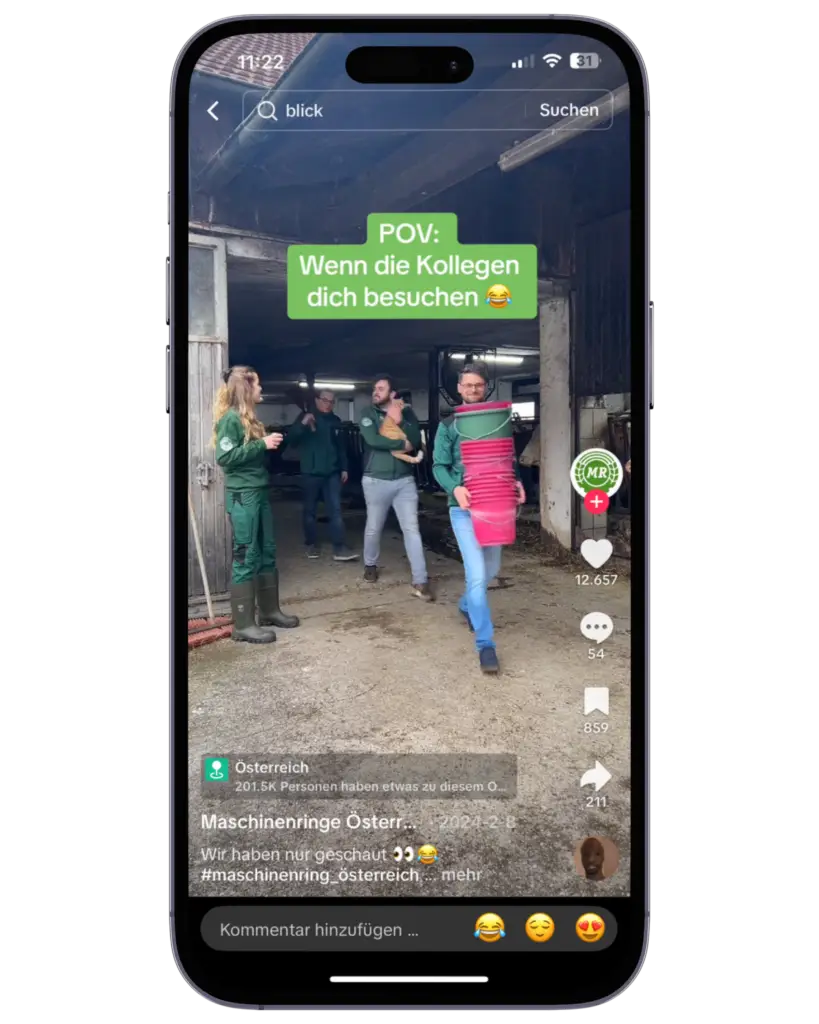 Ein TikTok-Video wird auf einem Smartphone gezeigt. Darin sind mehrere Personen in Arbeitskleidung vor einem Stall zu sehen, eine Person trägt eine Schürze.