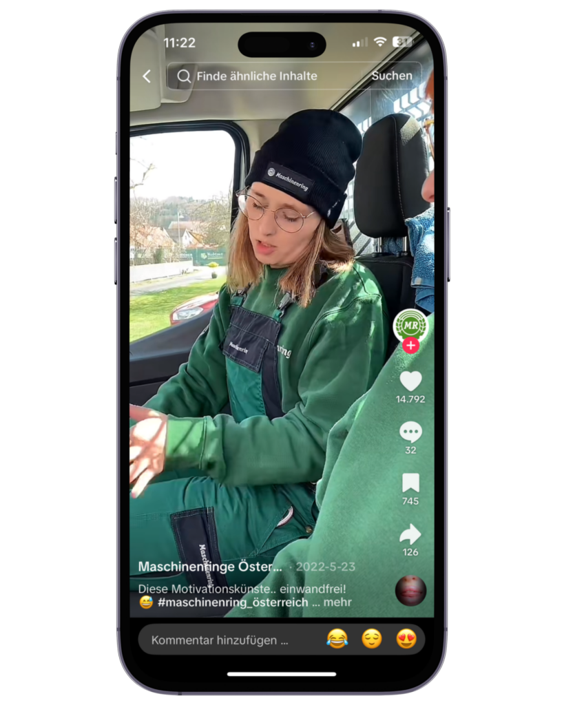 Eine junge Frau in grüner Arbeitskleidung und schwarzer Mütze mit „Maschinenring“-Logo sitzt in einem Fahrzeug und spricht.