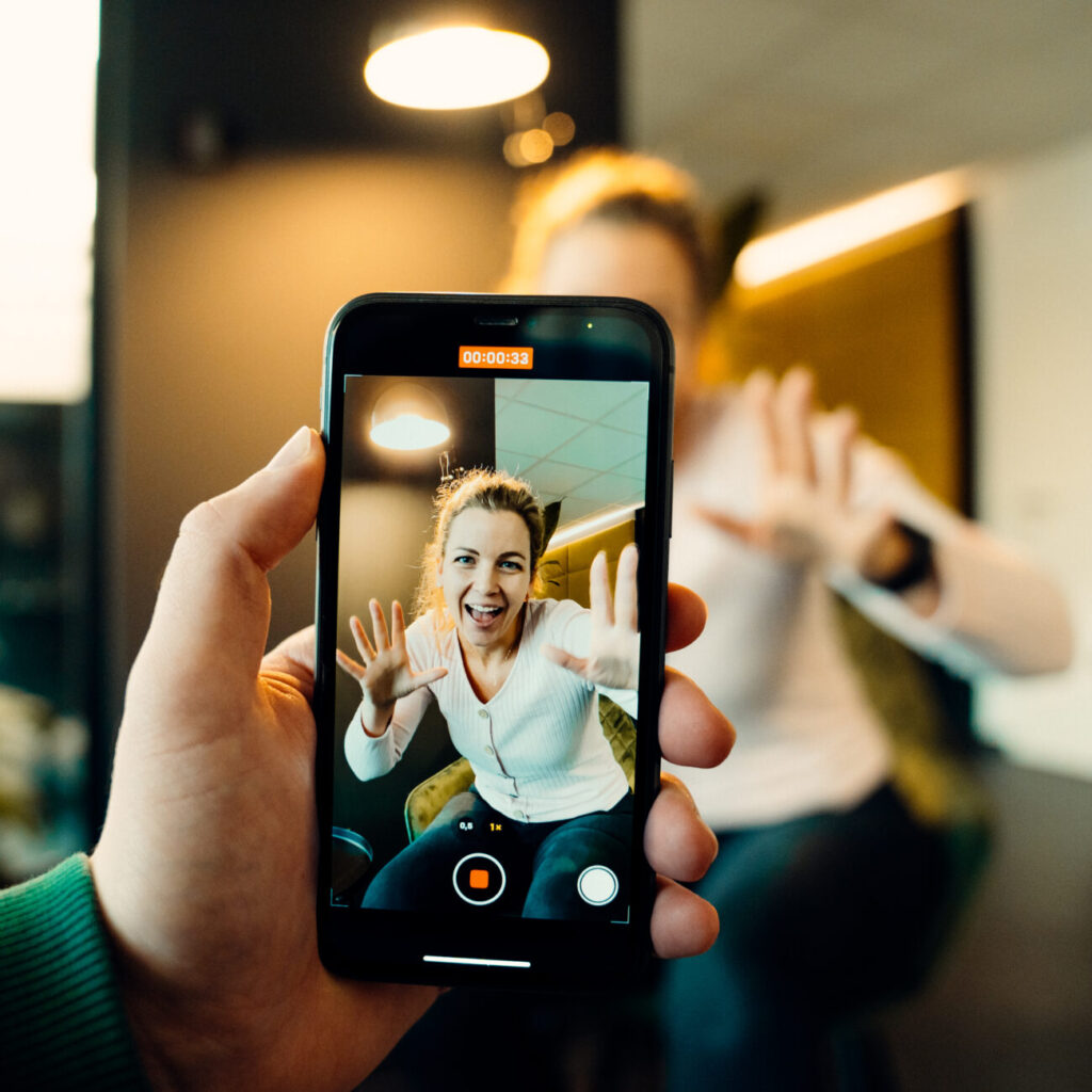 Smartphone filmt eine Frau im Büro – sie hält die Hände zur Kamera