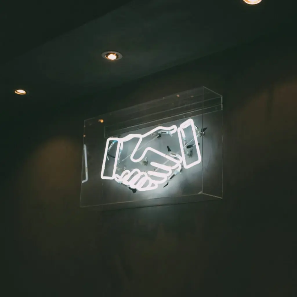 Leuchtendes Handschlag-Symbol als Neon-Schild an der Wand.