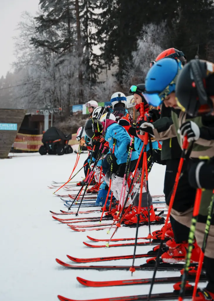 Kinder stehen mit Skiern auf einer Skipiste in einer Reihe