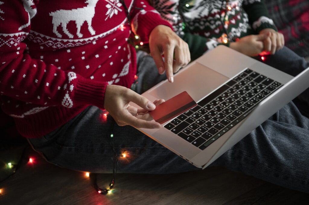Person im Weihnachts-Pullover kauft mit Kreditkarte online auf einem Laptop.