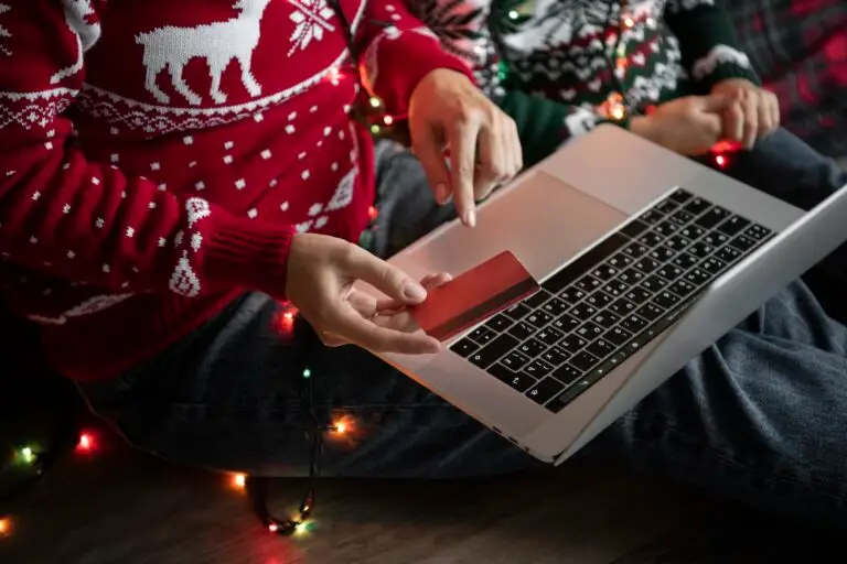Person im Weihnachts-Pullover kauft mit Kreditkarte online auf einem Laptop.