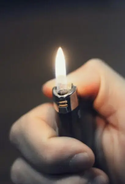 Hand hält ein Feuerzeug mit brennender Flamme.