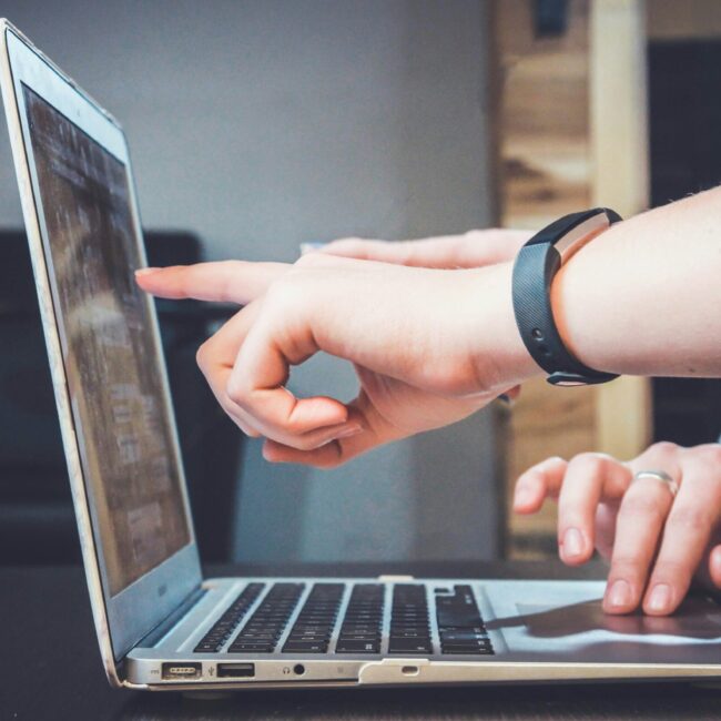 Person zeigt auf den Bildschirm eines Laptops, während eine andere Person tippt.