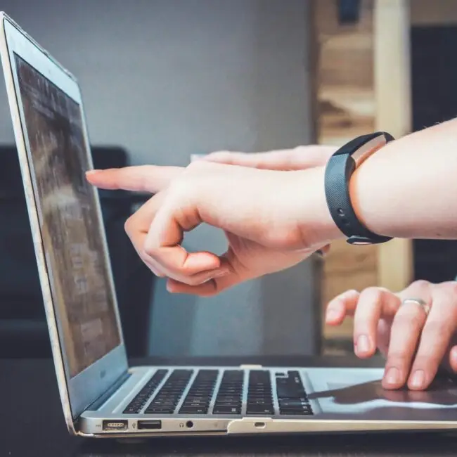 Person zeigt auf den Bildschirm eines Laptops, während eine andere Person tippt.