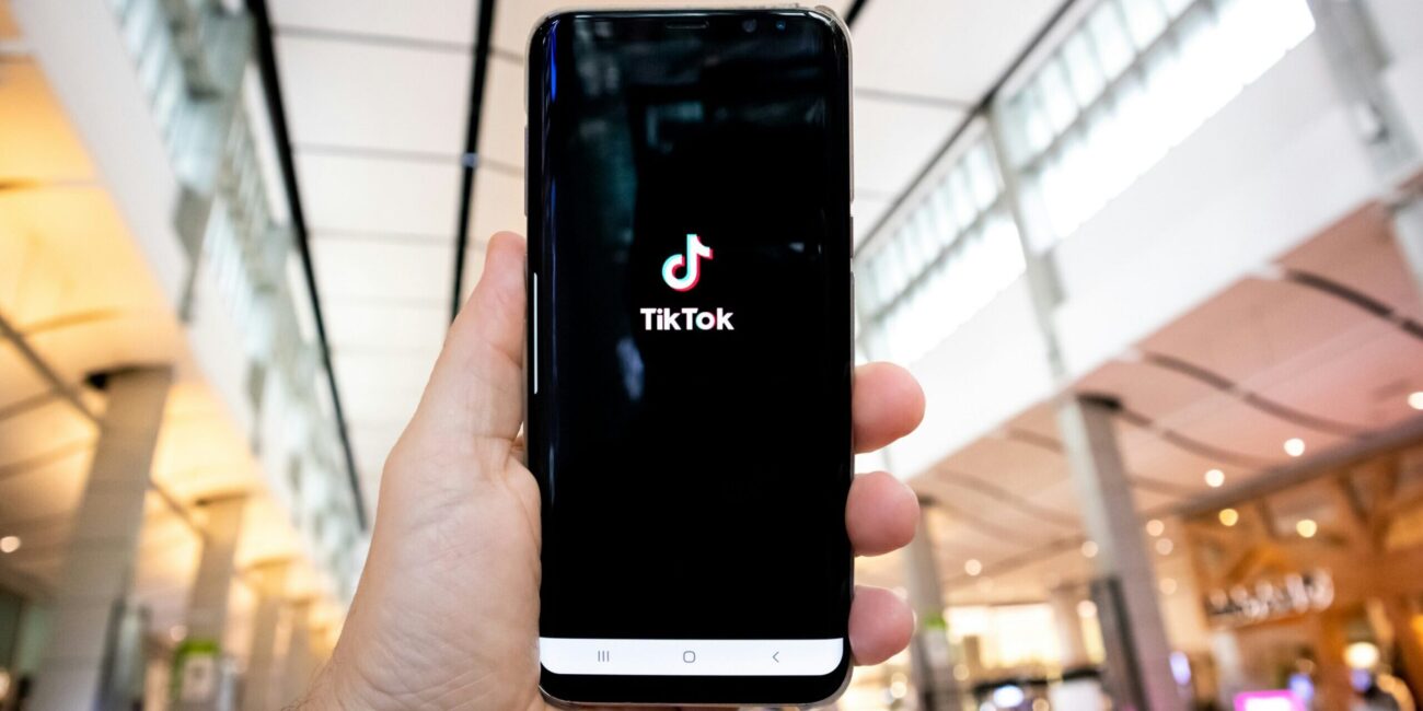 Hand hält ein Smartphone mit geöffneter TikTok-App.