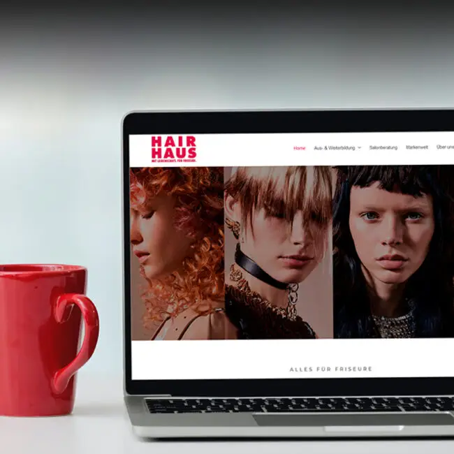 Geöffneter Laptop mit der Website von Hair Haus, auf dem drei Porträts mit unterschiedlichen Frisuren gezeigt werden. Daneben steht eine rote Kaffeetasse.