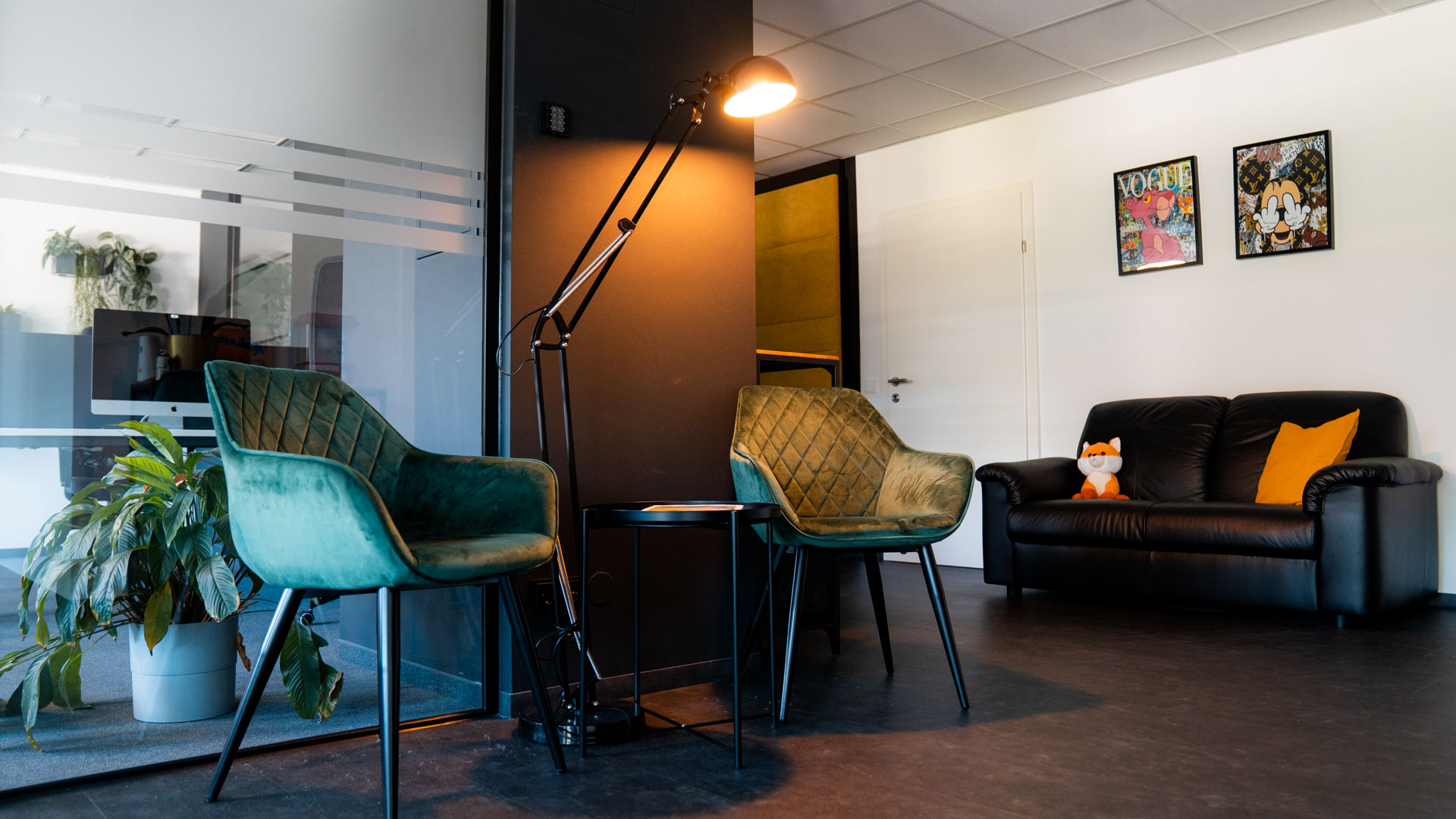 Wartebereich mit grünen Sesseln, schwarzem Sofa und Fuchs-Plüschtier.