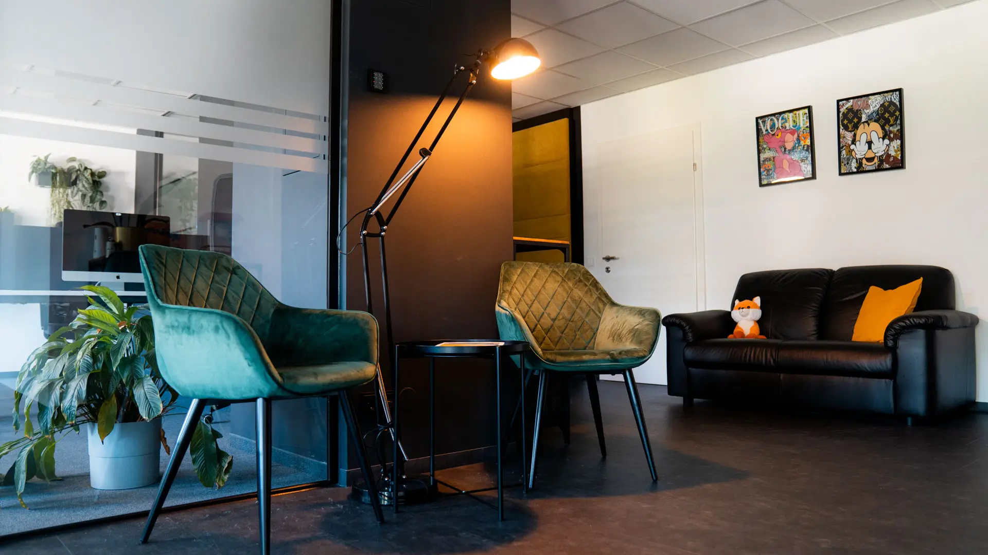 Wartebereich mit grünen Sesseln, schwarzem Sofa und Fuchs-Plüschtier.