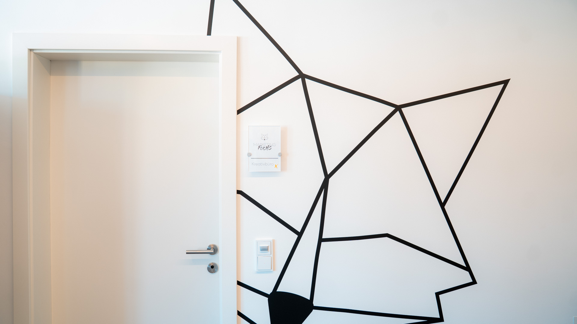 Weiße Bürotür mit kreativem Fuchs-Wanddesign und Firmenschild.