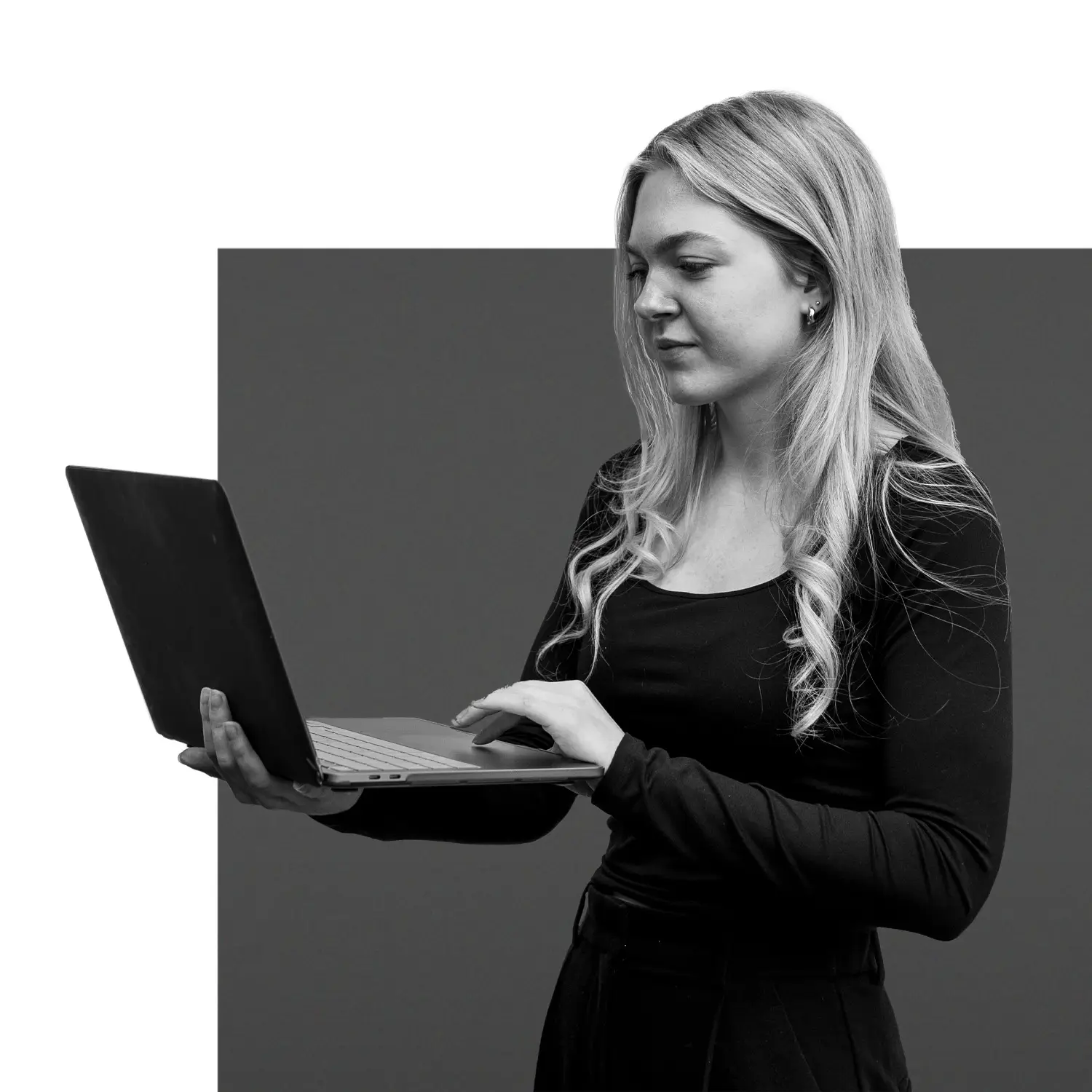 Schwarz-weiß Porträt einer jungen Frau im Profil, die im Stehen an einem Laptop arbeitet.