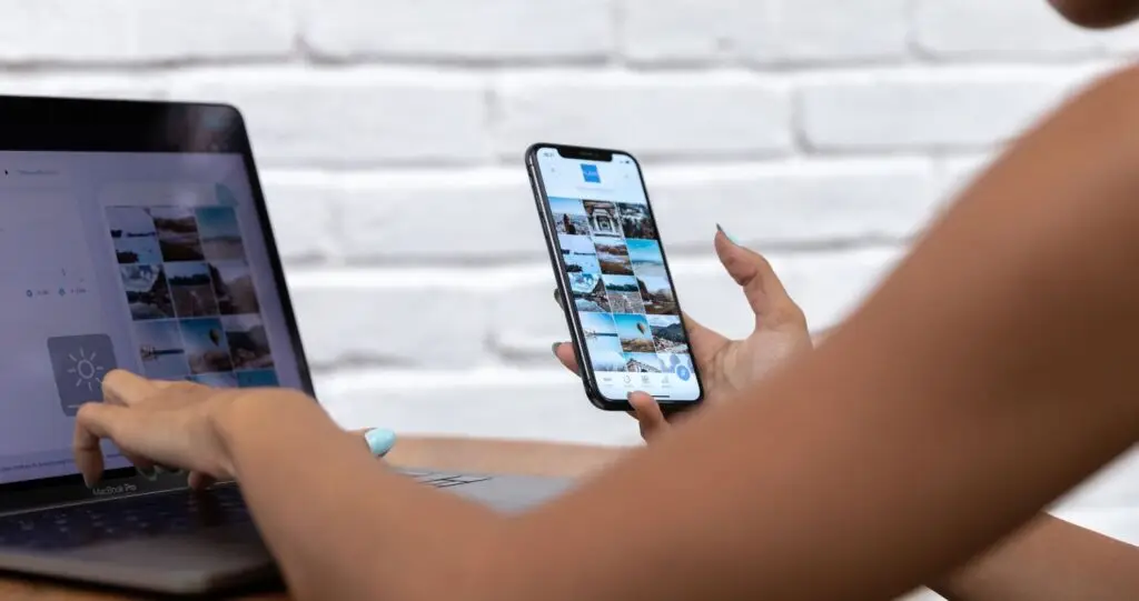 Bild am Beginn des Beitrages - zeigt eine Person, die mit einer Hand auf dem Laptop tippt und mit der anderen das Handy hält.